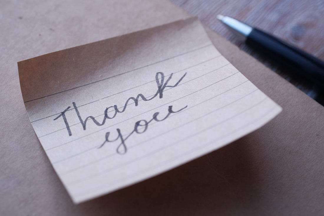 Close-up of a handwritten thank you note on brown paper with a pen nearby.