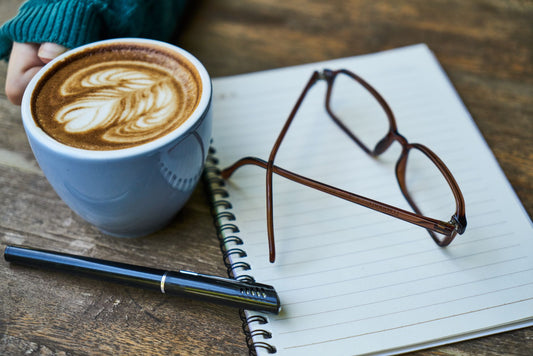 Cozy workspace featuring latte art, notebook, and glasses, perfect for creative thoughts.