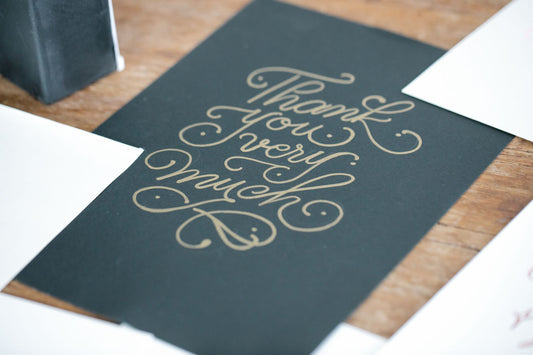 Close-up of a stylish thank you card with handwritten script on a wooden table.