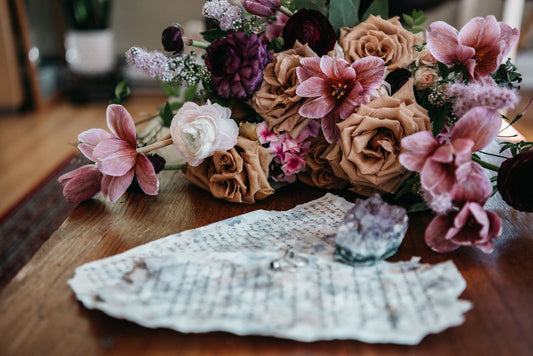 A delicate arrangement of mixed flowers with blurred handwritten notes on a wooden table.